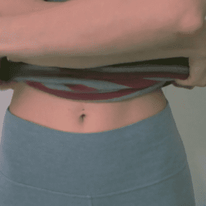 woman wearing grey yoga pants and removing striped tank top before filming the tampon fetish