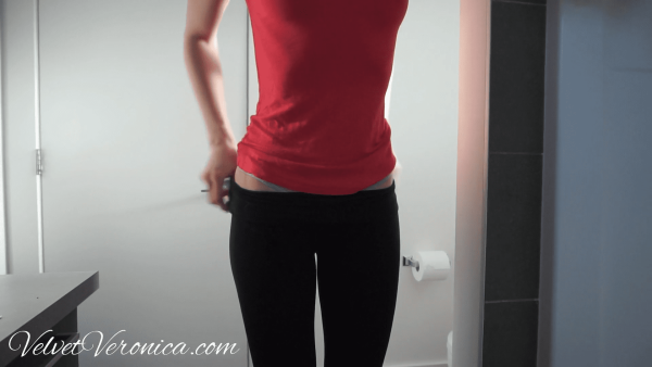 woman wearing pink shirt and black yoga pants before she starts peeing in a jar